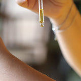 Une pipette d'huile jaune-verte au-dessus d'un avant-bras