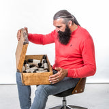 Sébastien Chabal assis sur une chaise avec une malle de produits Au Poil posée sur les genoux