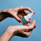 Sur un fond bleu ciel, on voit une main qui appuie sur la pompe du gel relaxant anal pour montrer la texture du gel sur un doigt