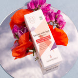 Un étui en carton de sérum anti-âge rétinal 0.1% de la marque Clémence & Vivien, posé sur un miroir avec quelques fleurs roses et des coquelicots