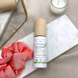 Sur un tissu écru, une plaque de marbre est posée avec un chouchou satiné rose, une bougie et un miroir. Un flacon de soin visage Cosmoz est posé sur la plaque de marbre