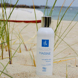 Sur une plage de sable fin, un flacon d'eau micellaire de la marque Passion Marine, dont la base est enfoncée dans le sable