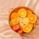 Sur un drap satiné, est posée une passoire avec des tranches d'agrumes