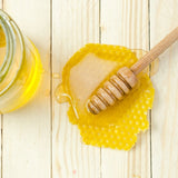 Une cuillère à miel avec du miel posée sur du parquet en bois très clair