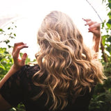 Une femme aux cheveux blonds et bouclés vue de dos dans un champ