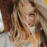 Une femme blonde, les cheveux au vent, elle porte un pull beige