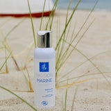 Un flacon d'exfoliant doux visage de la marque Passion Marine, posé sur une plage de sable fin