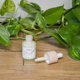 Un flacon-pipette du sérum anti-imperfections de la marque Cosmoz posé sur du parquet, la pipette est couchée à droite du flacon. En arrière-plan, des feuillages.