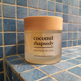 Dans une salle de bain carrelée en bleu, un pot en verre d'huile de coco Coconut Rhapsody de la marque My Mira est posé