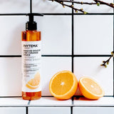 Dans une salle de bain en carrelage blanc, une huile de douche senteur orange douce de la marque Phytema