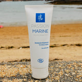 Un tube de masque purifiant à la boue marine et aux actifs marins de la marque Passion Marine, posé sur un mur avec une plage en arrière-plan
