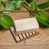 Un savon Cosmoz au miel de Manuka posé sur un élément en bois ajouré sur un parquet avec des feuillages autour