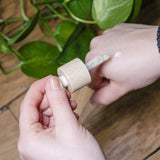 Une personne montre la texture du sérum anti-imperfections Cosmoz sur le dos de sa main droite à l'aide de la pipette. En arrière-plan on voit du parquet avec une plante grasse type Monstera