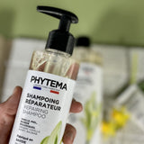 Gros plan sur un flacon-pompe de shampoing réparateur de la marque Phytema tenu par une main