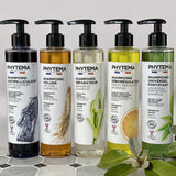 5 shampoings Phytema posés sur de la faïence grise, de gauche à droite : antipelliculaire, volume, réparateur, séborégulateur et universel fortifiant.