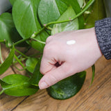 Une goutte de soin hydratant Cosmoz au miel de Manuka sur le dos d'une main de femme avec en arrière-plan du parquet et les feuilles d'une plante grasse type Monstera