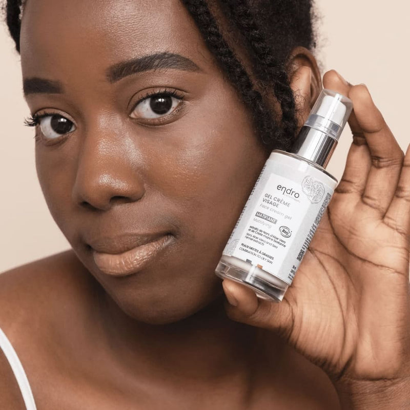 Une femme à la peau noire tient un flacon de gel crème visage matifiant de la marque Endro