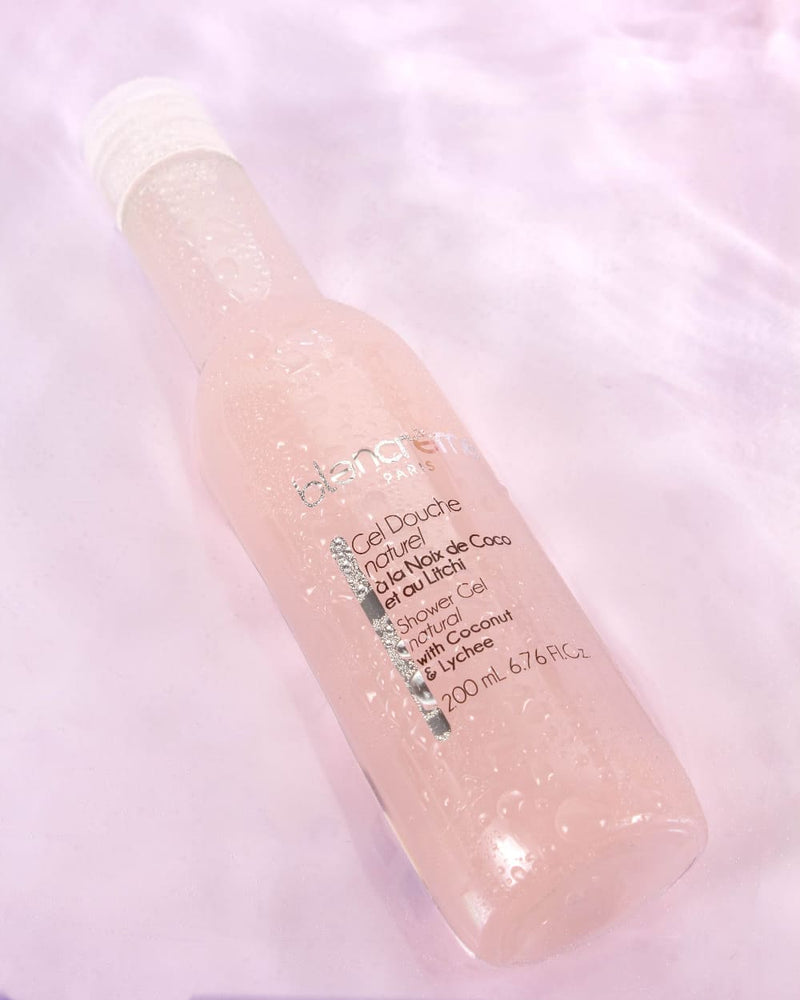 Sur un fond rose clair, un flacon de gel douche Blancrème de senteur noix de coco et litchi
