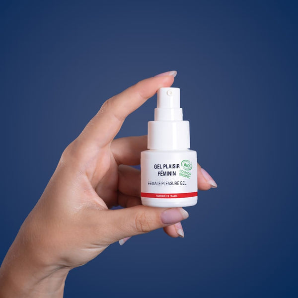 Sur fond bleu, une main de femme tient un petit flacon de gel plaisir féminin de la marque Goliate