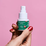 Sur un fond rose, une main de femme avec du vernis à ongles rouge tient un flacon de gel relaxant anal de la marque Goliate