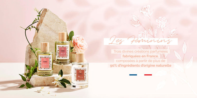 Un sol écru avec un mur rose pâle orné d'ombres légères. A gauche 3 flacons d'eaux de toilette pour femme de la marque Siobhan : Inattendu, Eternal et Precious. Ils sont présentés devant une pierre en travertin et entourés de feuillages et fleurs. A droite, un texte explique qu'elles sont fabriquées en France et composées à partir de plus de 90% d'ingrédients d'origine naturelle
