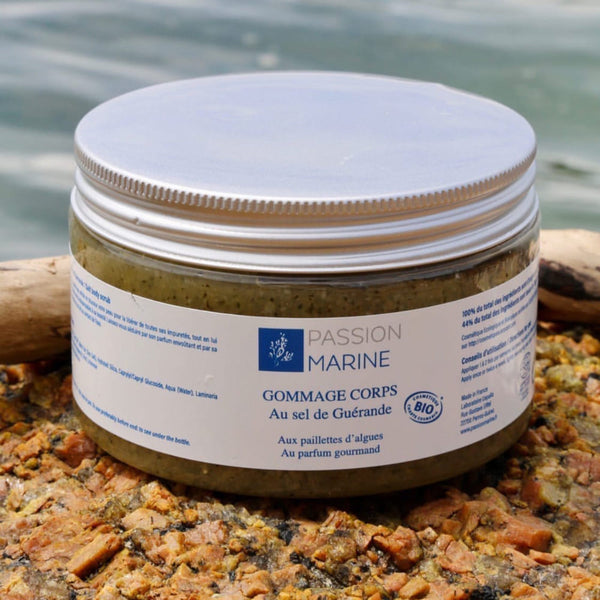 Sur une plage bretonne avec l'océan en arrière-plan, un pot de gommage corps au sel de Guérande de la marque Passion Marine