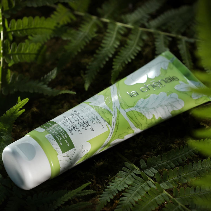 Sur un fond de feuillages verts foncés, un tube de crème moussante de la marque La Chênaie est couché