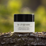 Dans un fond naturel, une crème nutritive intense de la marque La Chênaie est posée sur un tronc d'arbre avec un fond vert flouté qui suggère des arbres feuilletés